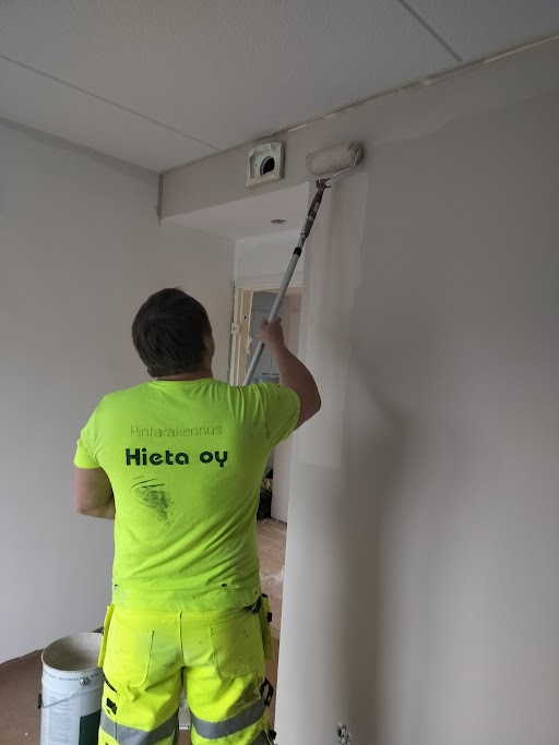 Aleksei maalaa seinää telalla Pintarakennus Hieta Oy:n työvaatteissa.