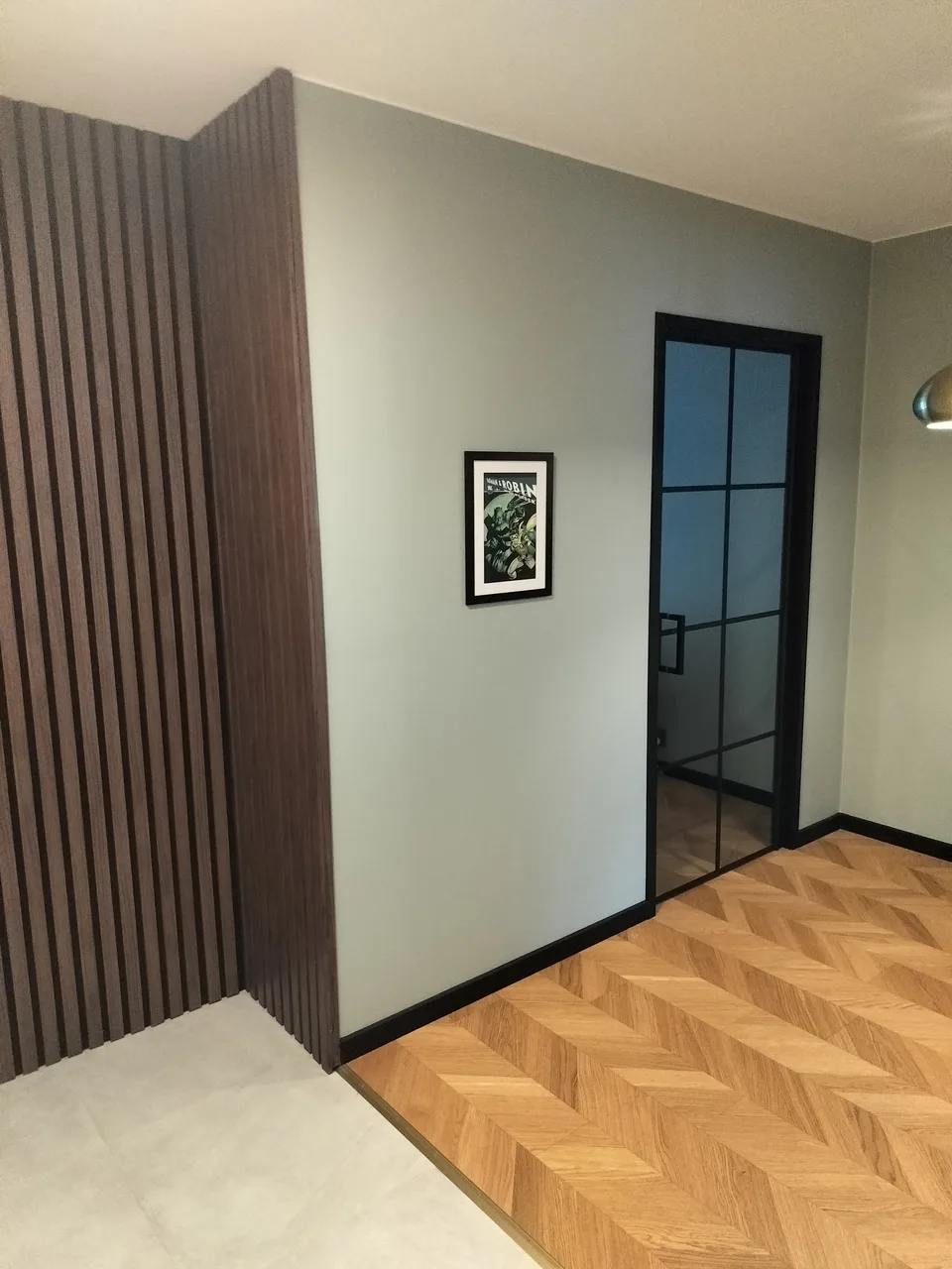 Eteisen puulattia, rimaseinä ja mustakehyksinen lasiovi.